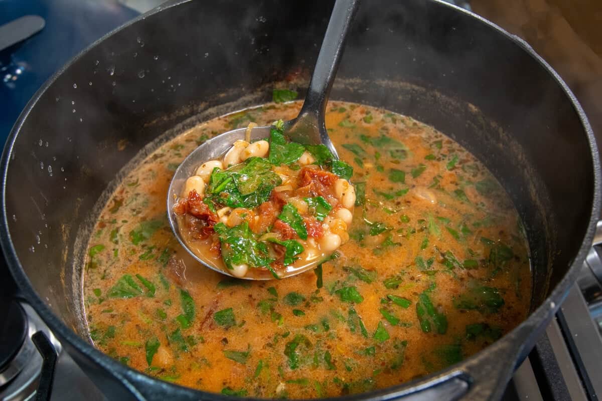 large pot of marry me bean soup with a ladle scooping some out