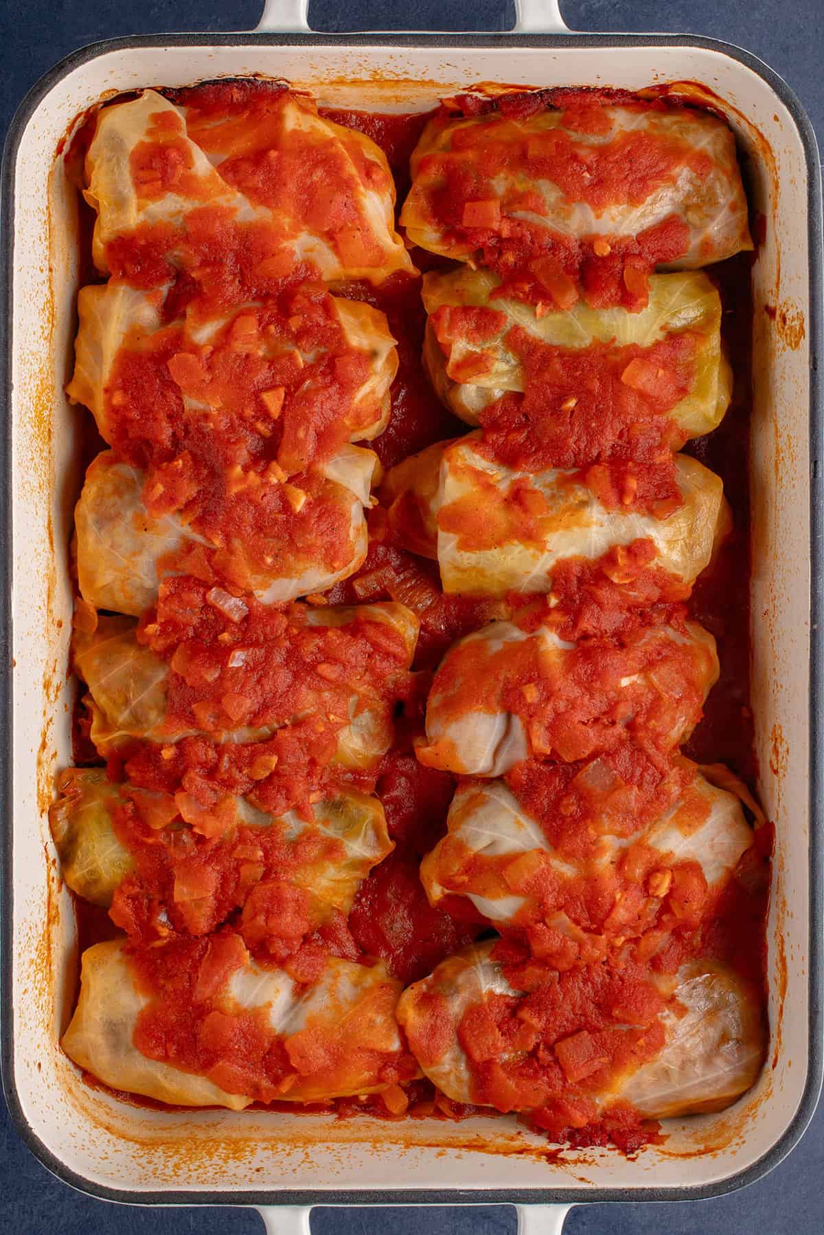overhead of stuffed cabbage rolls lined up in a baking dish topped with tomato sauce after baking