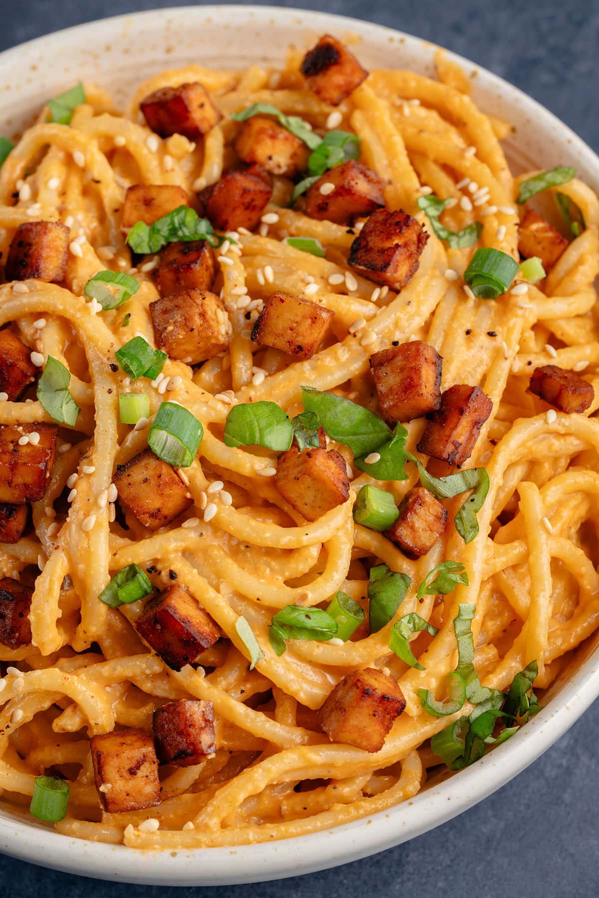 bowl of gochujang carbonara on blue background topped with green onions and sesame seeds