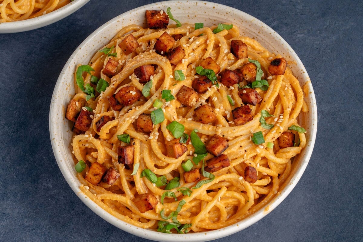 bowl of gochujang carbonara on blue background topped with green onions and sesame seeds
