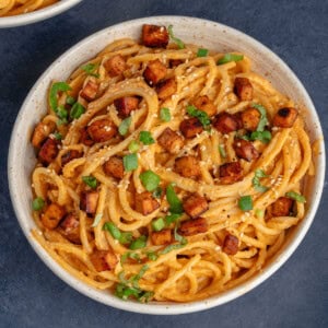 bowl of gochujang carbonara on blue background topped with green onions and sesame seeds