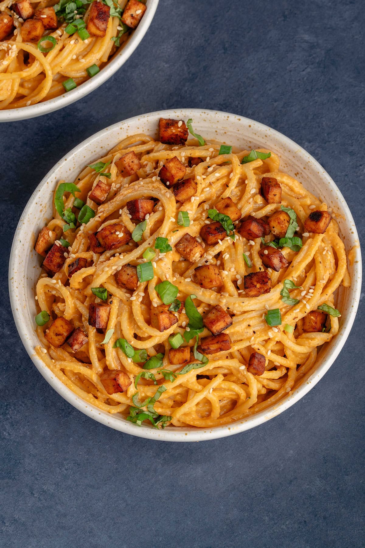 bowl of gochujang carbonara on blue background topped with green onions and sesame seeds