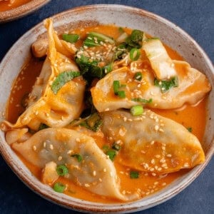 bowl of red curry dumplings topped with sesame seeds and scallions