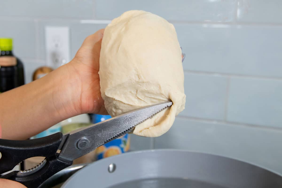 cutting the tofu pasta dough with scissors into a pot