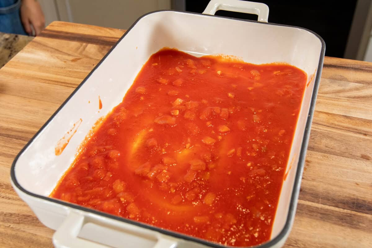 adding sauce to the bottom of a baking dish