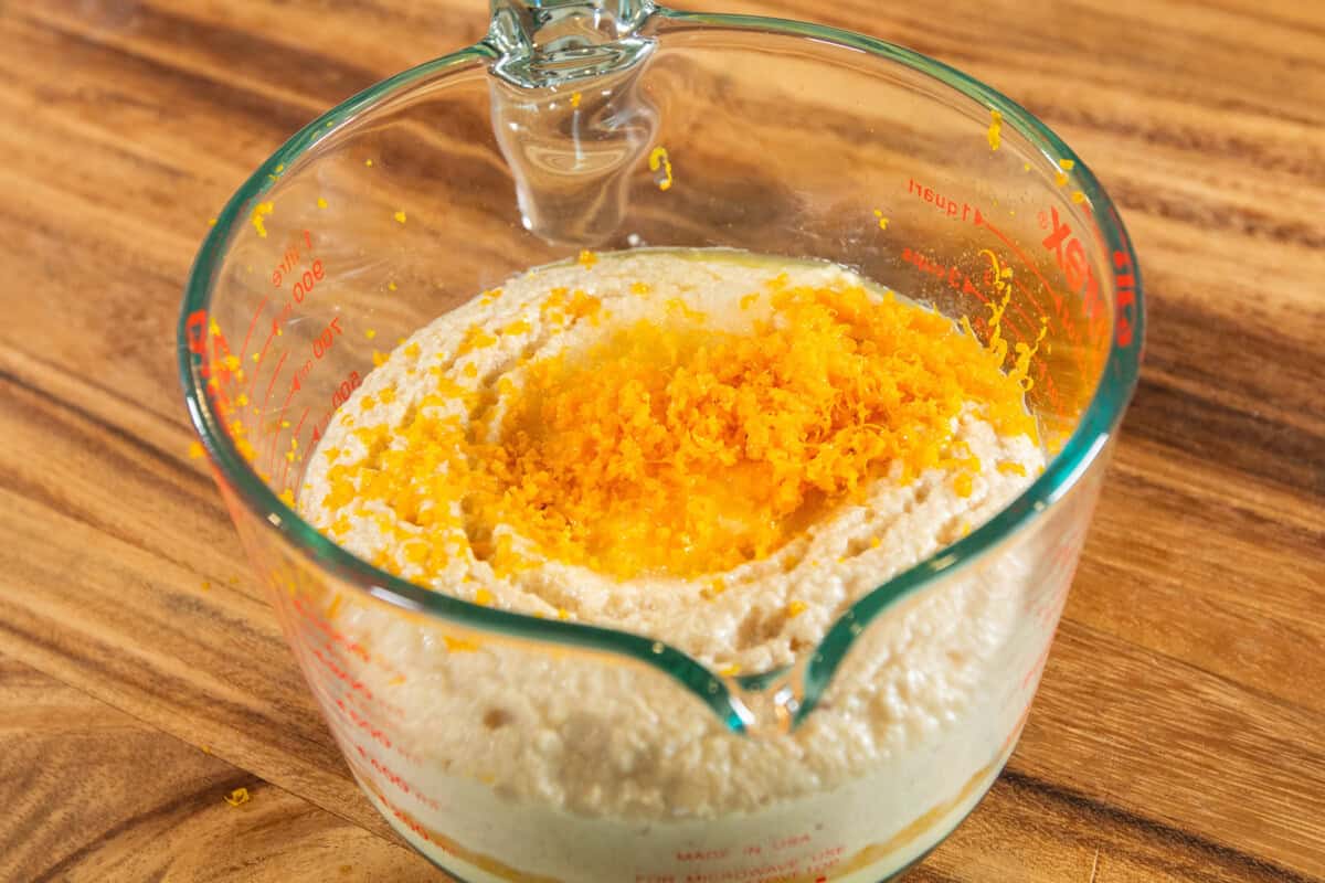 adding orange zest to yeast mixture in measuring cup