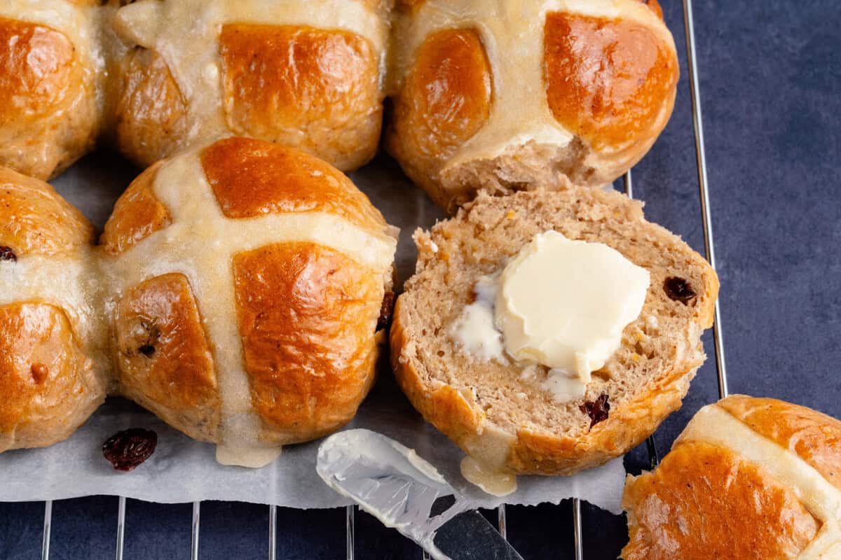 row of hot cross buns with one cut in half at the end with butter on it