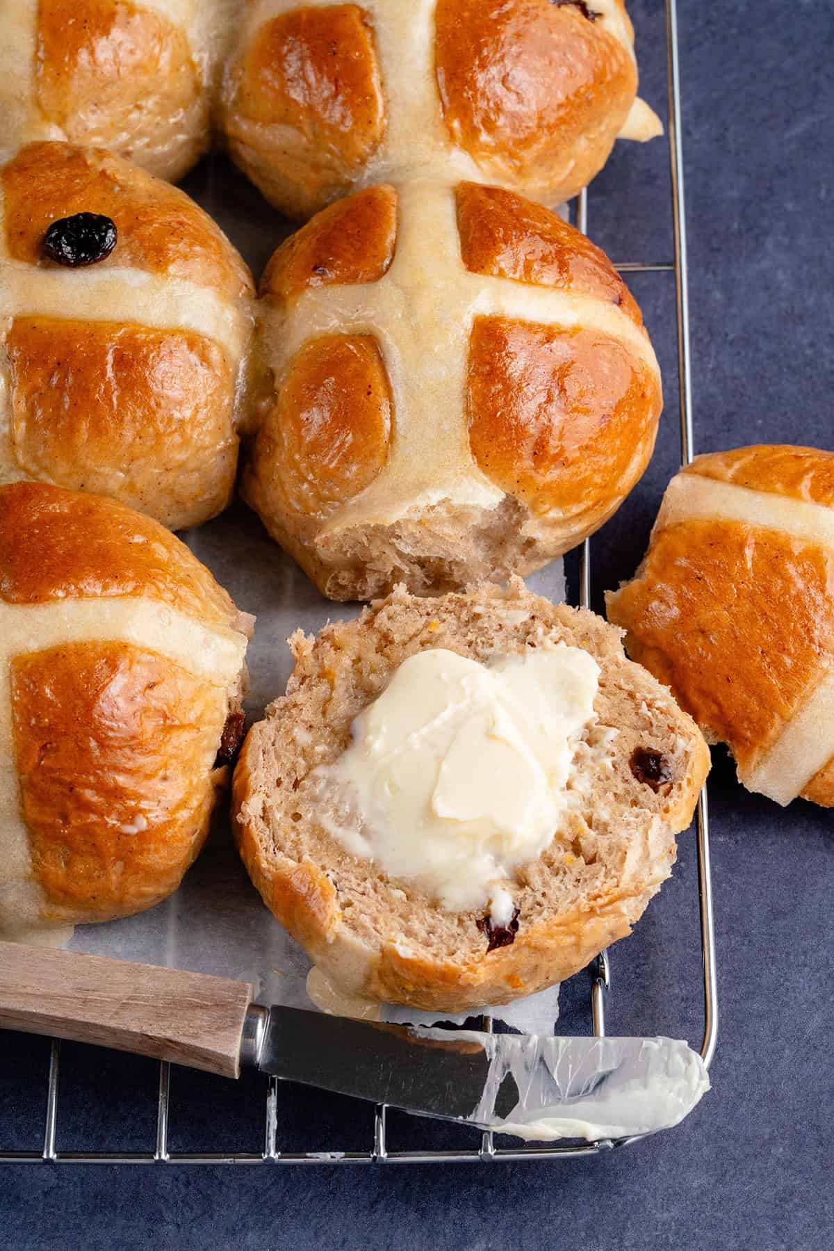 vegan hot cross buns cut in half with a pat of butter spread on the open side