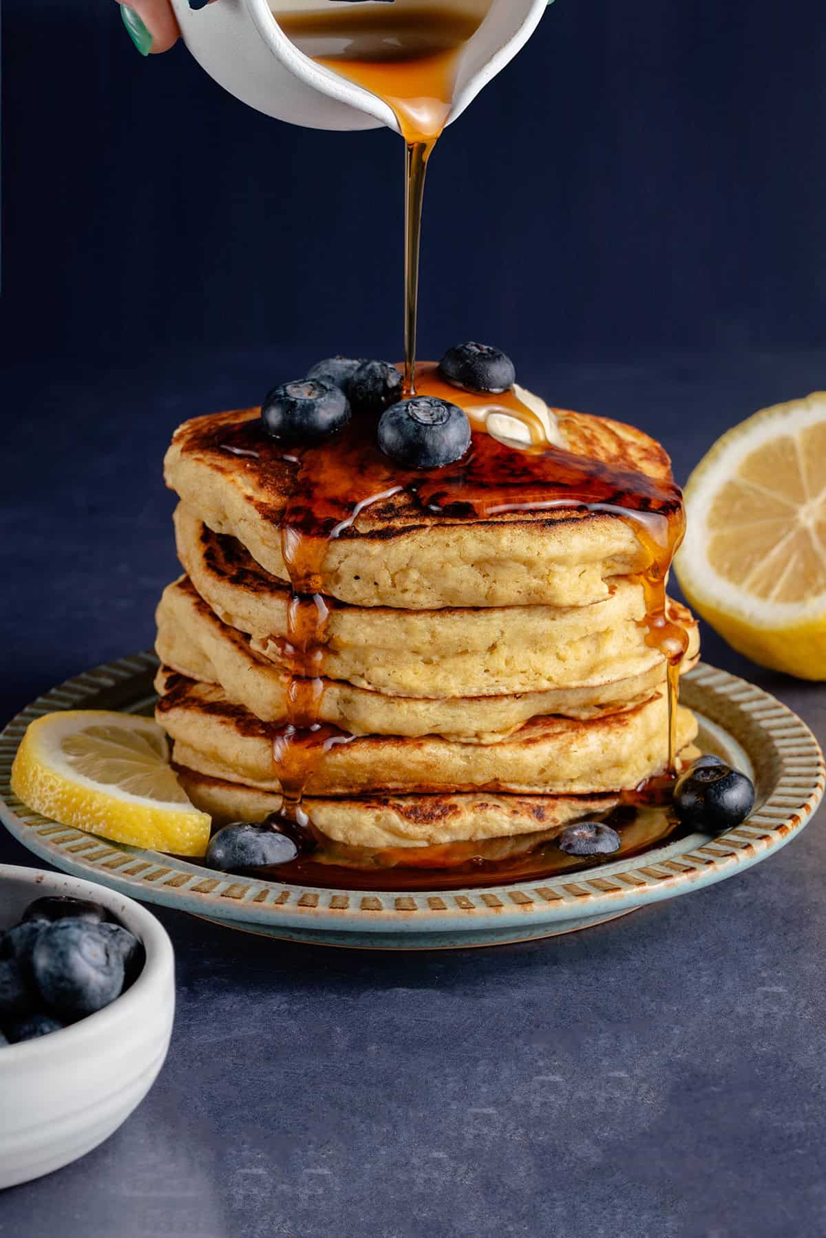 pouring syrup over stack of lemon ricotta pancakes