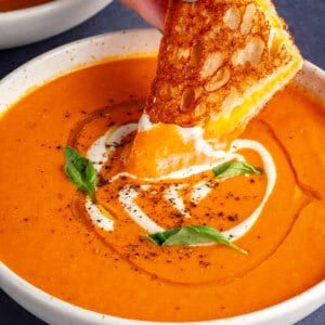 dipping grilled cheese into bowl of creamy vodka tomato soup