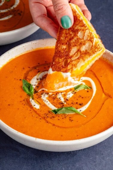 dipping grilled cheese into bowl of creamy vodka tomato soup