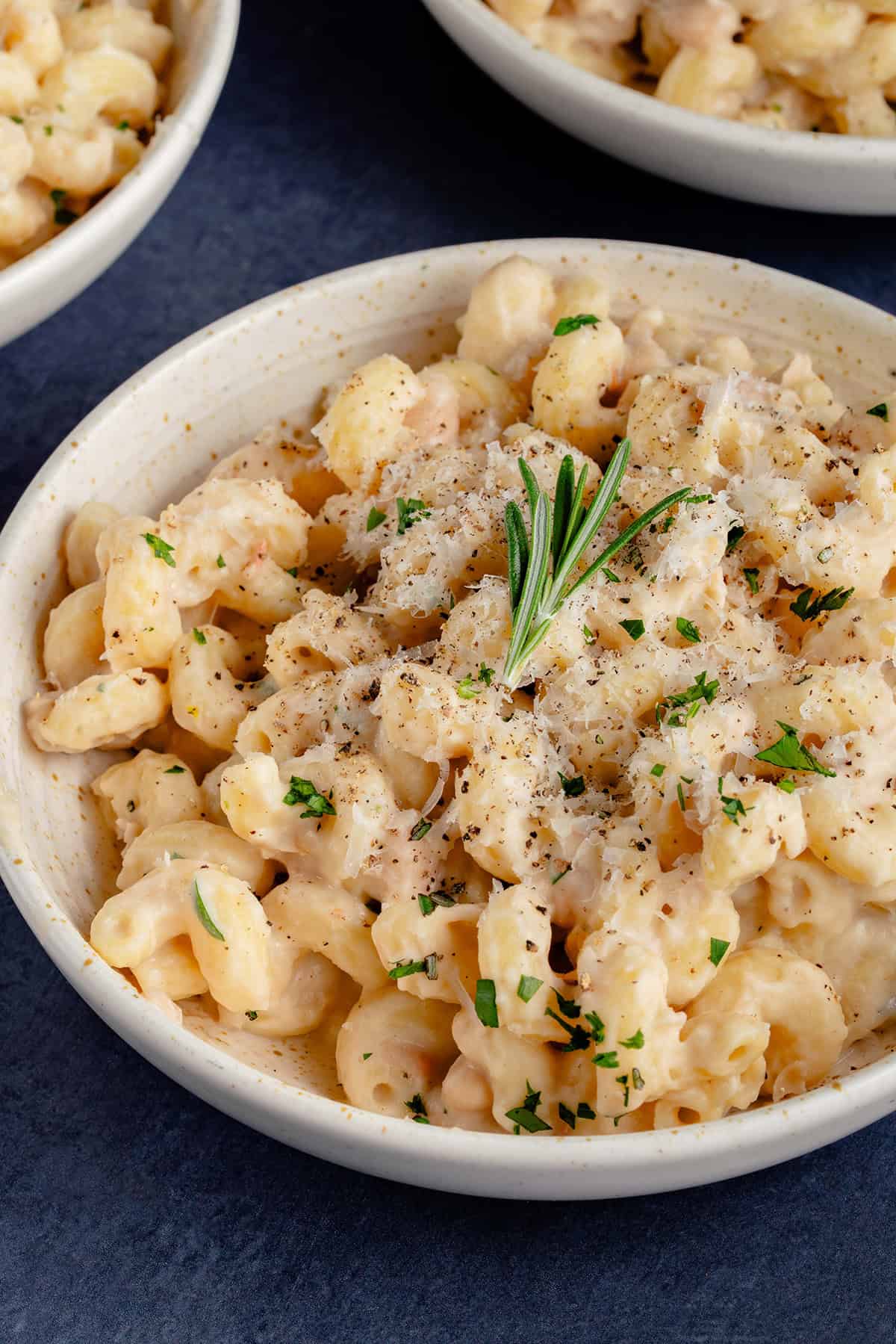 Creamy White Bean & Rosemary Pasta in a bowl topped with vegan parmesan and a sprig of rosemary