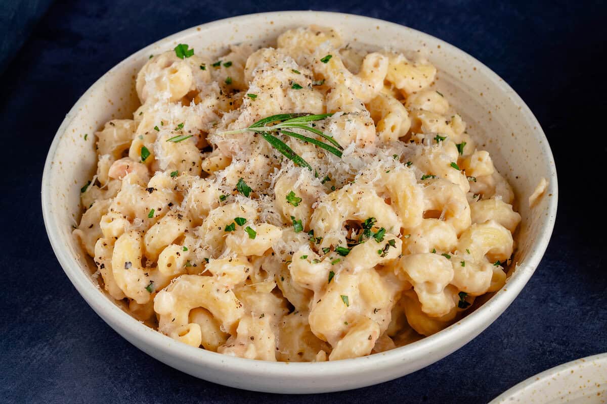 Creamy White Bean & Rosemary Pasta in a bowl topped with vegan parmesan and a sprig of rosemary