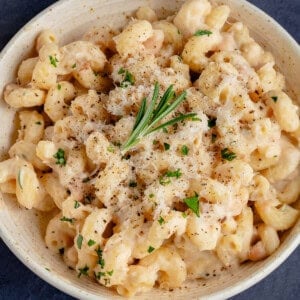 Creamy White Bean & Rosemary Pasta in a bowl topped with vegan parmesan and a sprig of rosemary