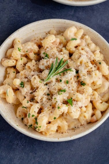 Creamy White Bean & Rosemary Pasta in a bowl topped with vegan parmesan and a sprig of rosemary