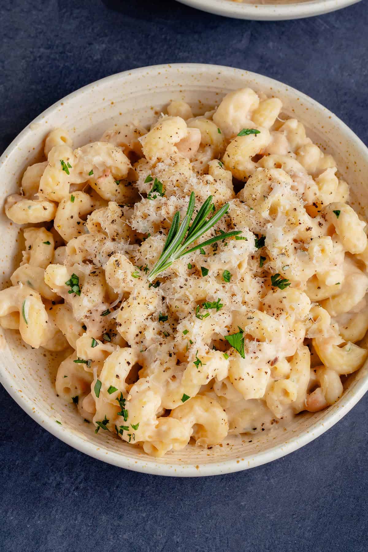 Creamy White Bean & Rosemary Pasta in a bowl topped with vegan parmesan and a sprig of rosemary