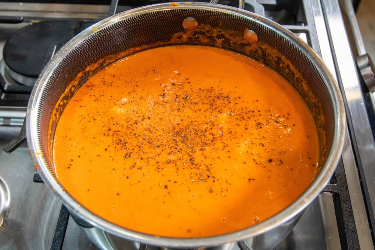 adding salt and pepper to pot of vodka tomato soup