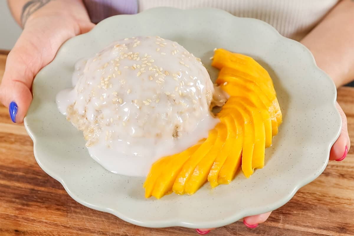 plate of finished mango sticky rice oatmeal topped with coconut sauce and a side of sliced mango