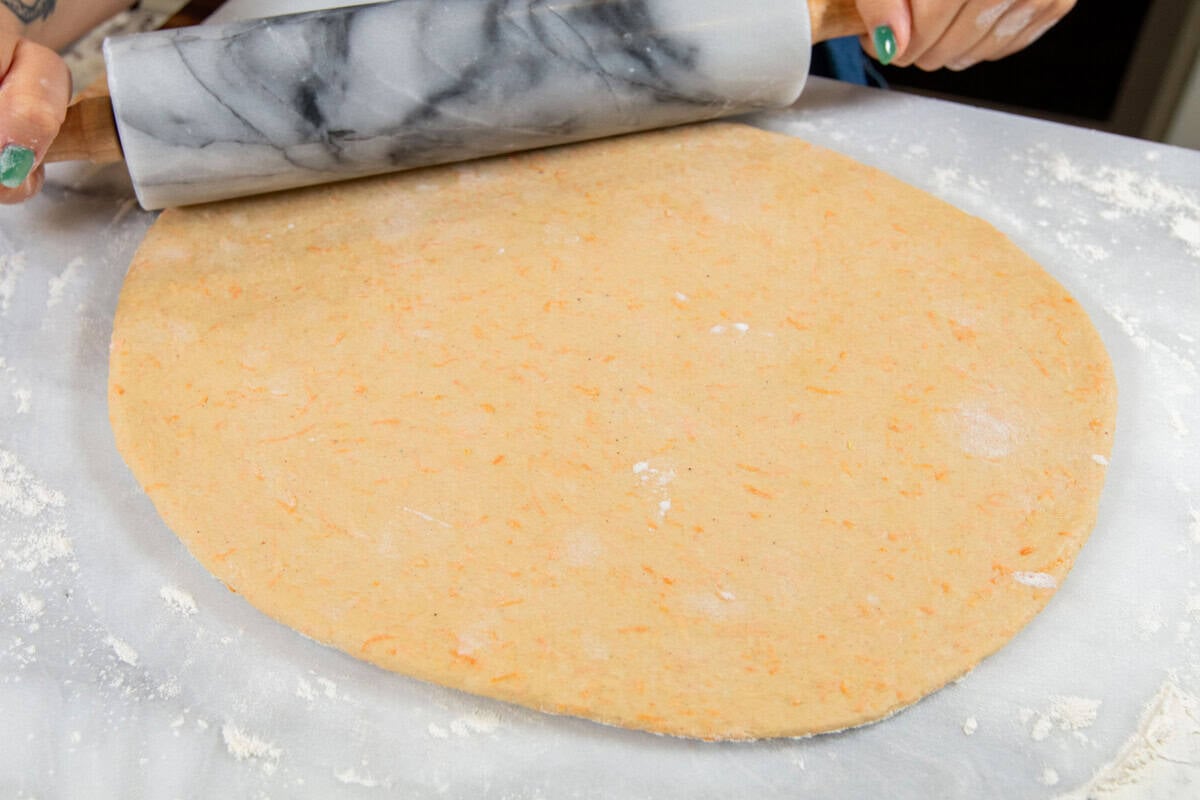 rolling out cinnamon roll dough with rolling pin on floured work surface