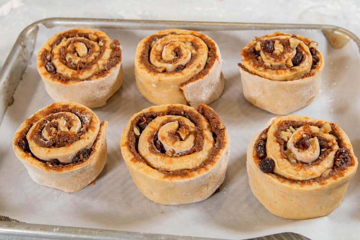 rolled carrot cake cinnamon rolls on lined baking sheet