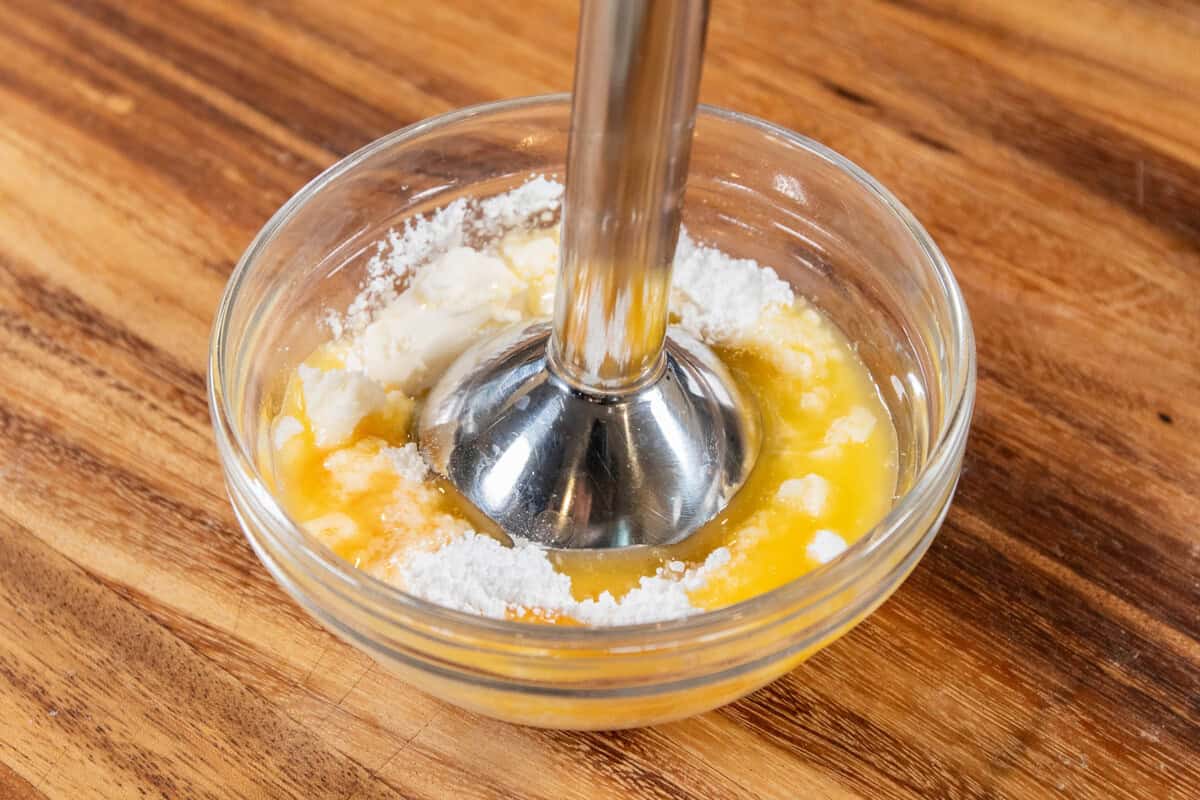 mixing cream cheese frosting in small bowl with immersion blender