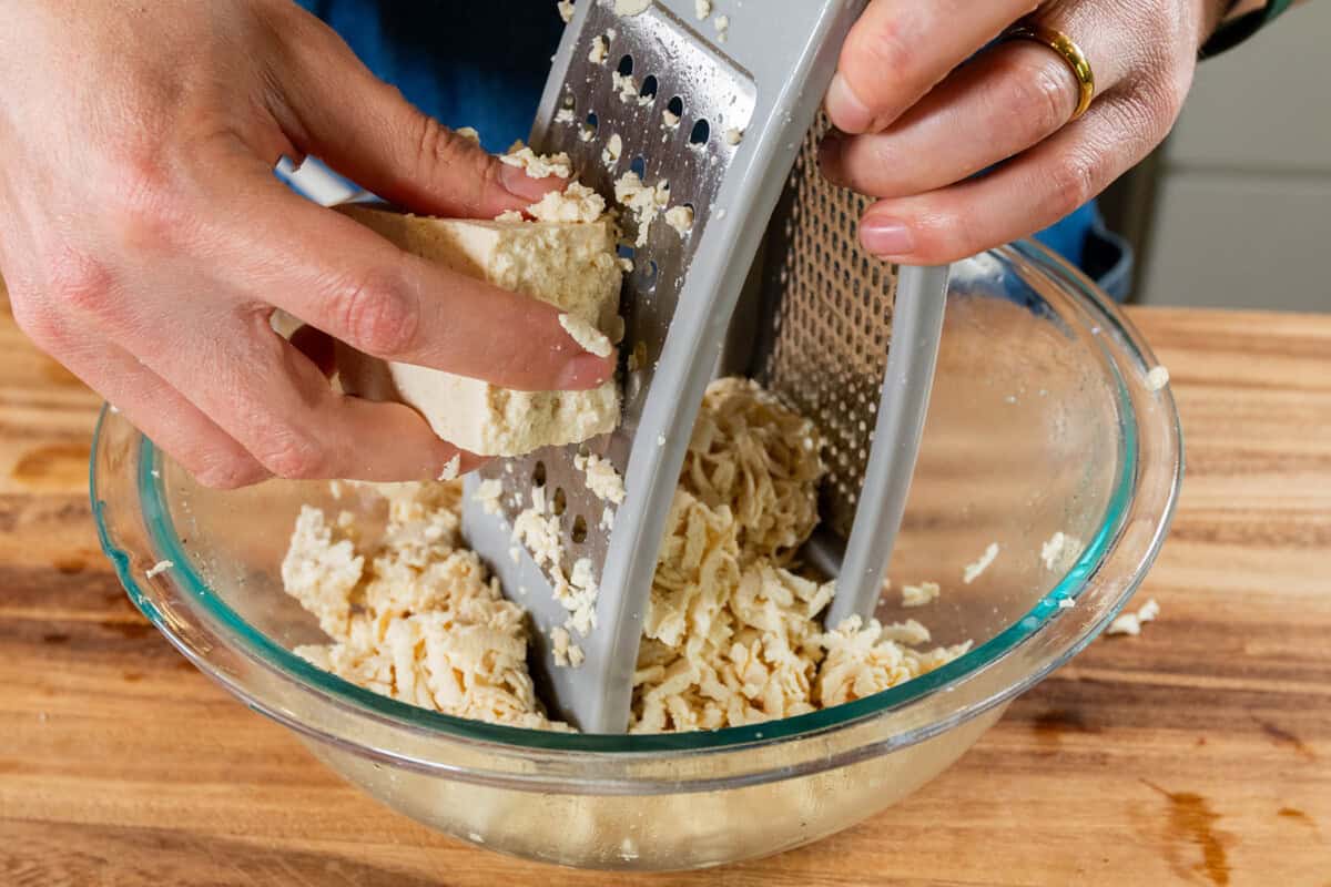 grating a block of tofu into large glass bowl