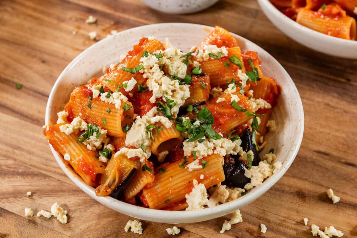 a white bowl of Pasta alla Norma (Eggplant Pasta) topped with tofu ricotta salata and fresh basil