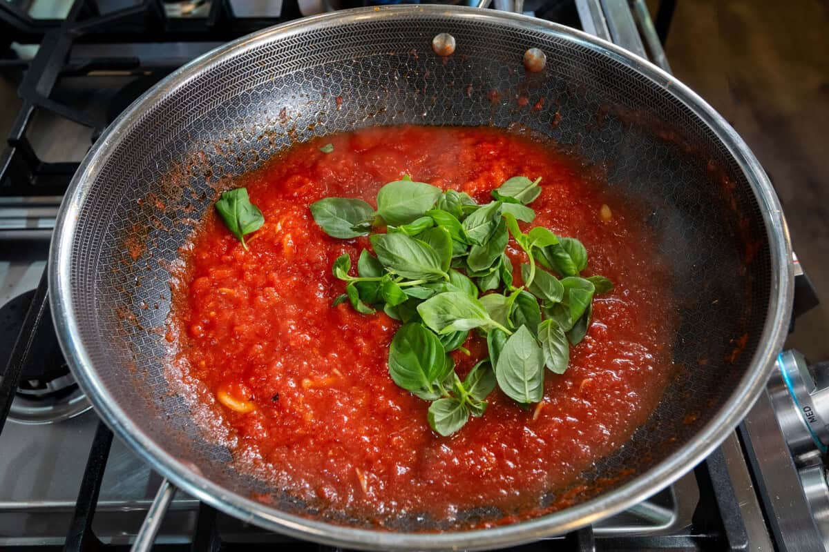 adding fresh basil to homemade tomato sauce for Pasta alla Norma (Eggplant Pasta) recipe
