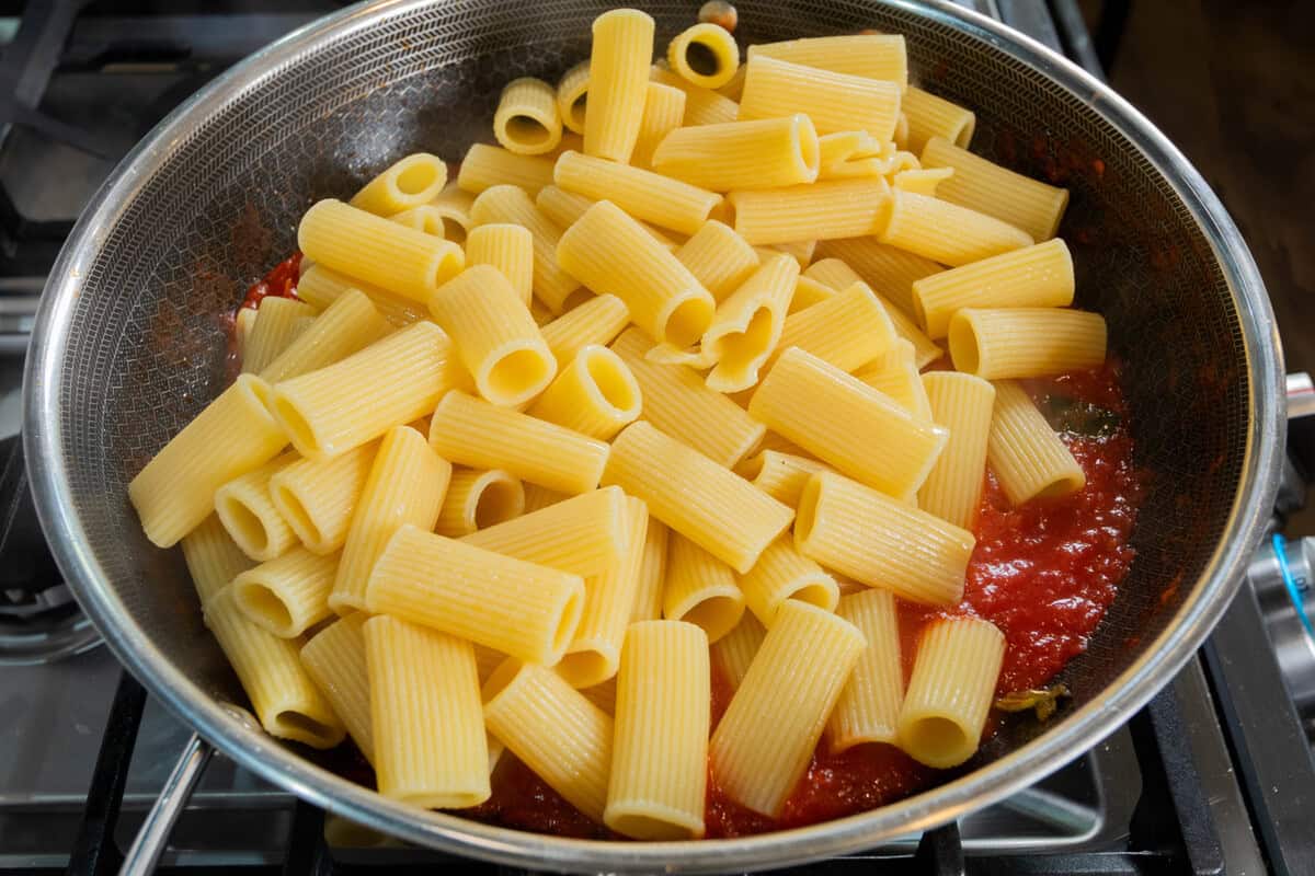 pasta being added to a pot of sauce for Pasta alla Norma (Eggplant Pasta)