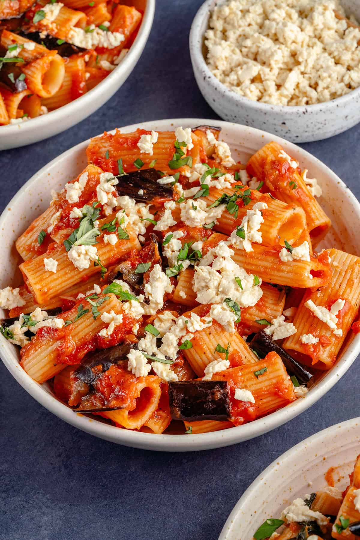 white bowl of Pasta alla Norma (Eggplant Pasta) topped with tofu ricotta salata and fresh basil