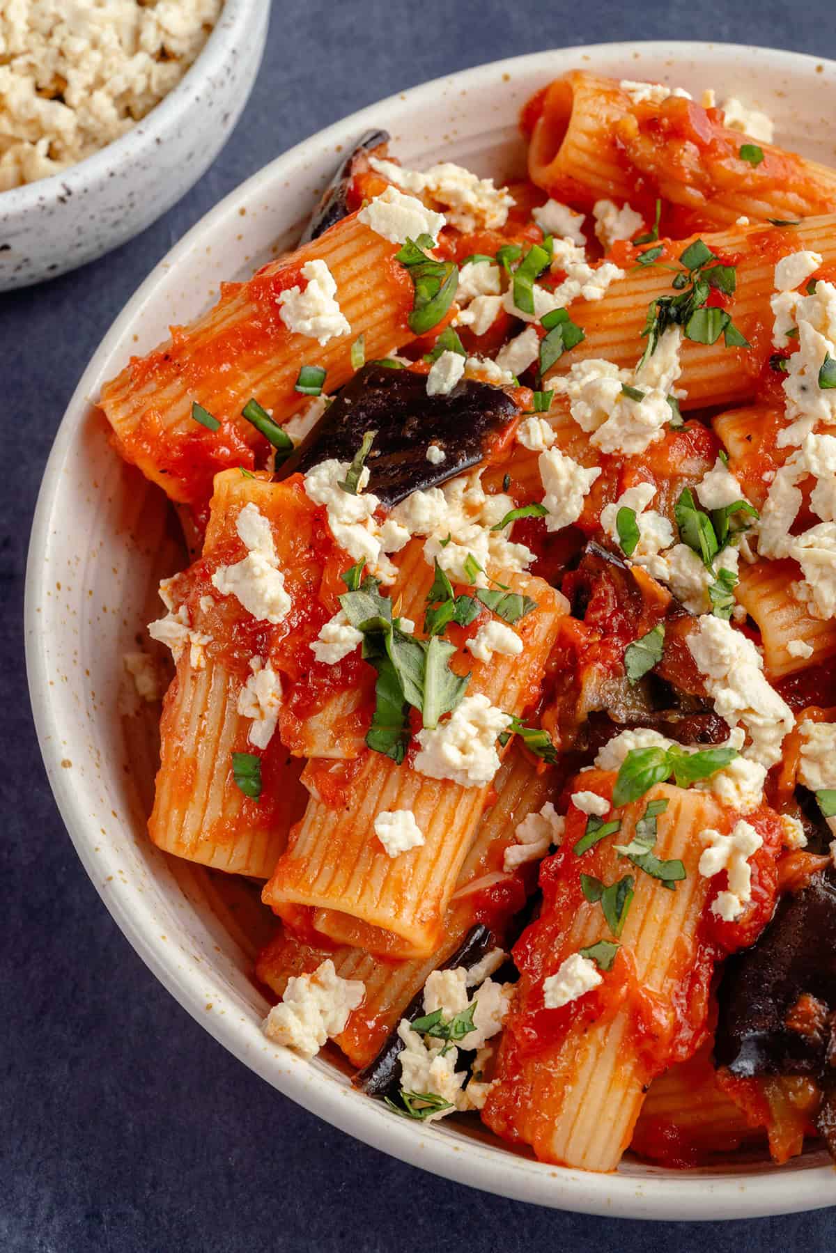 overhead photo of a white bowl of Pasta alla Norma (Eggplant Pasta) topped with tofu ricotta salata and fresh basil