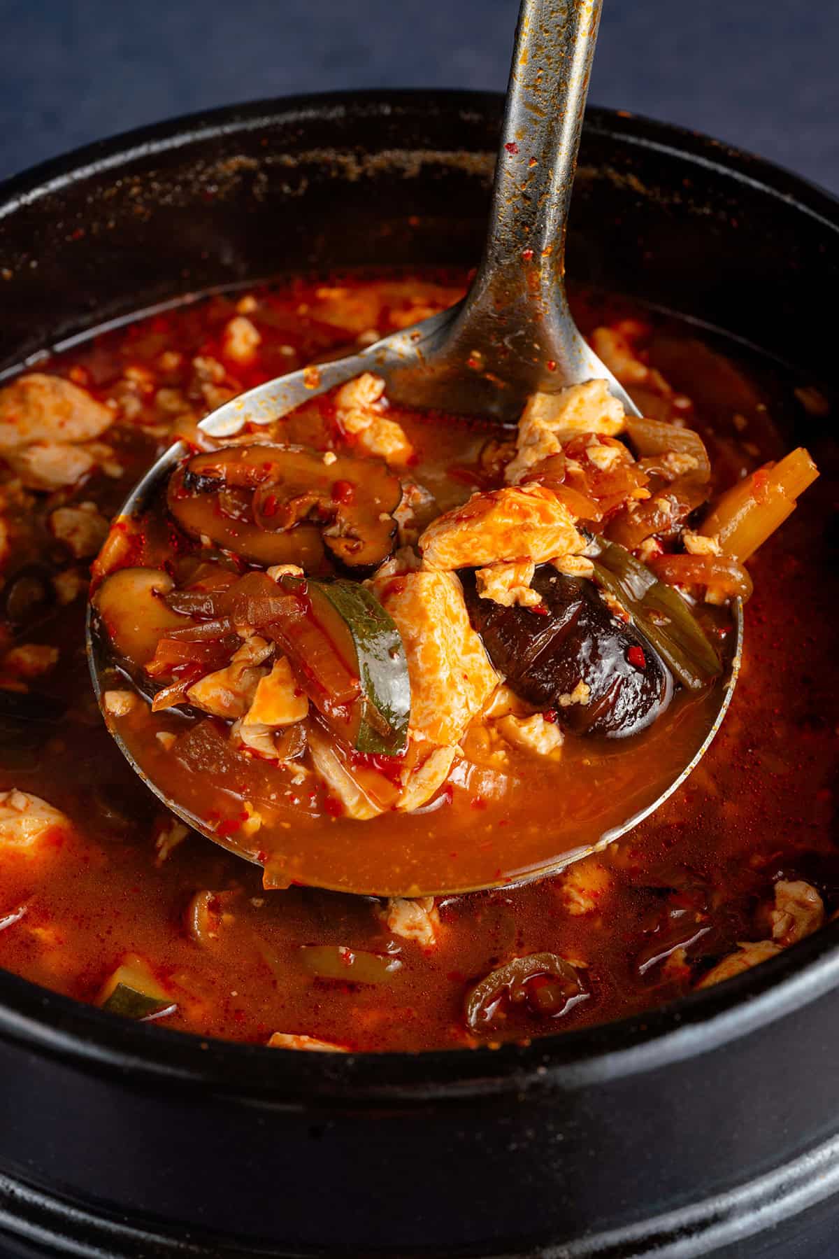 lifting Vegan Sundubu-Jjigae (Korean Soft Tofu Stew) out of pot with ladle