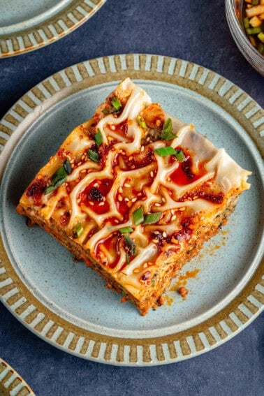 slice of lumpia-inspired dumpling lasagna on blue plate topped with chili oil, sawsawan, and green onions
