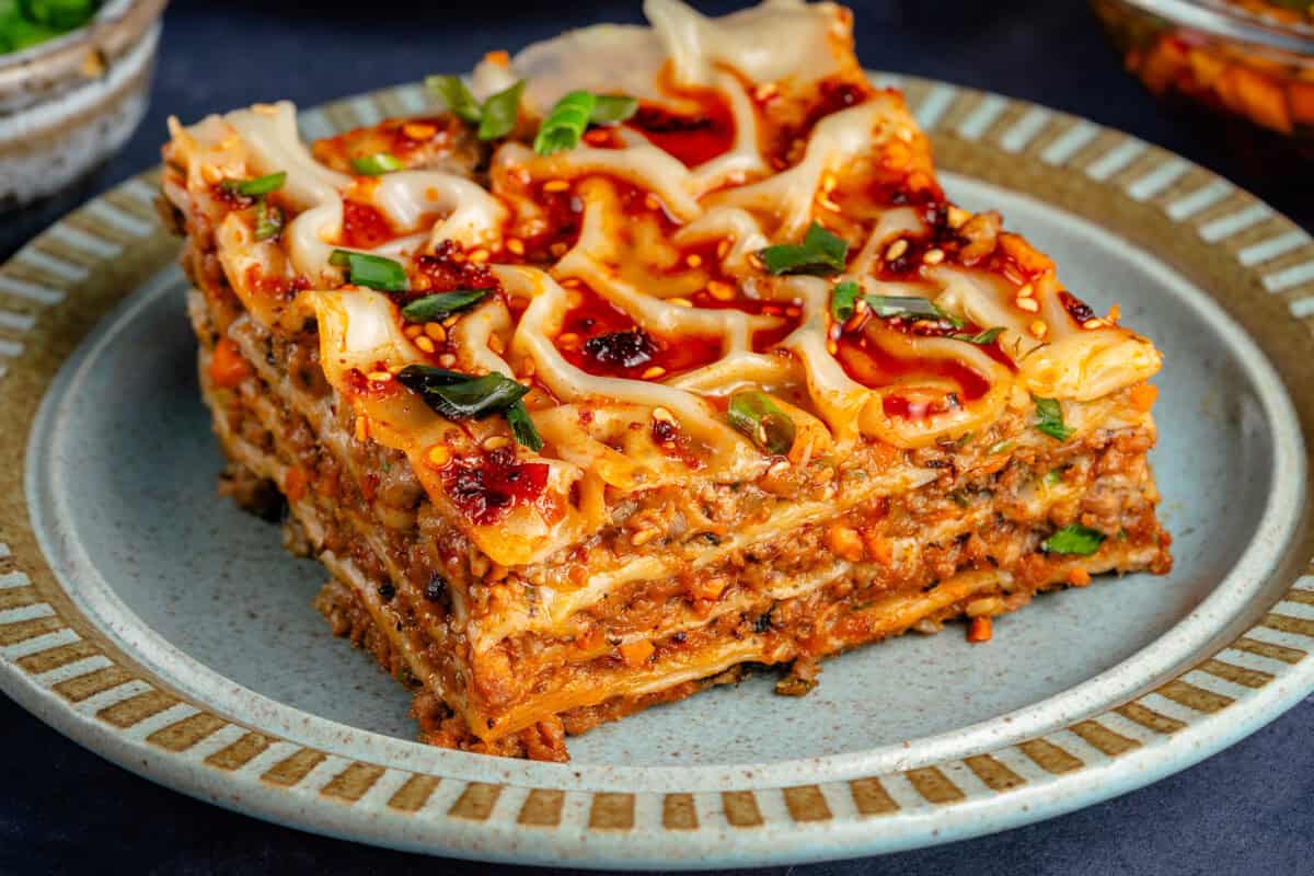 slice of lumpia-inspired dumpling lasagna on blue plate topped with chili oil, sawsawan, and green onions