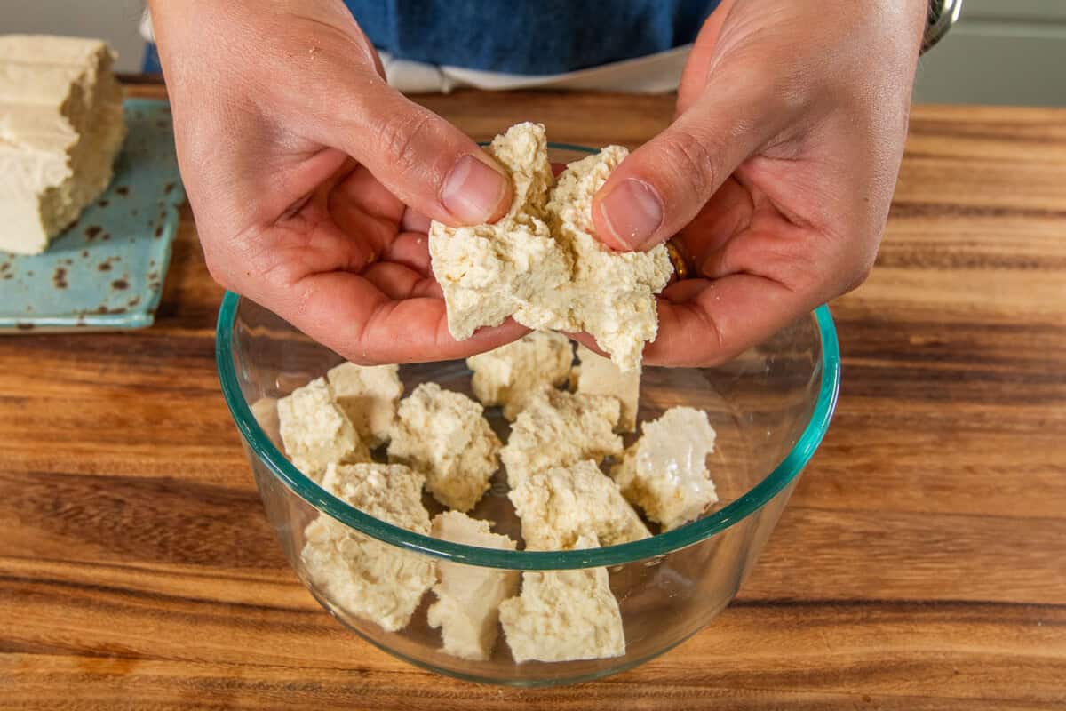 breaking apart tofu into a bowl