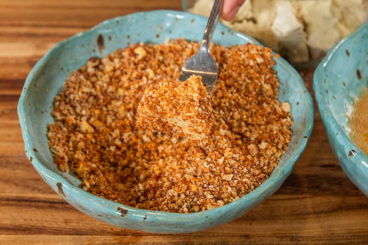 breaded tofu held by a fork over the bowl of breadcrumbs