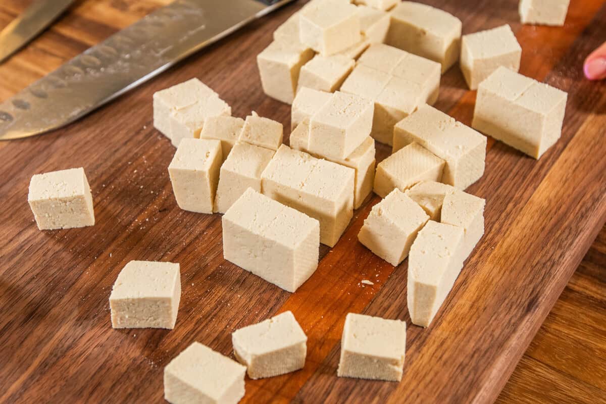 Vegan tofu cubes on a wooden cutting board with a knife, ready for cooking or seasoning.