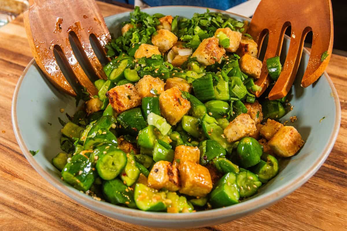 tossing the smashed cucumber salad in a blue bowl