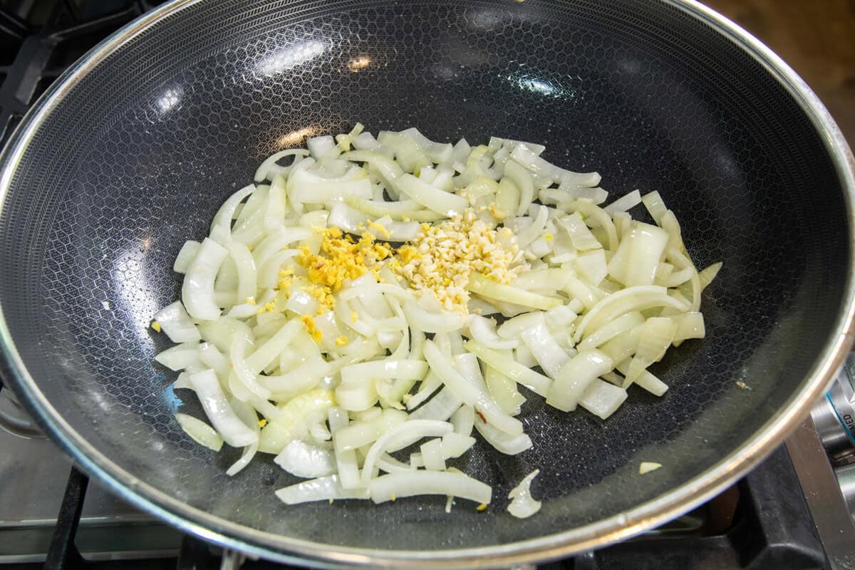adding garlic and ginger to the onions in a skillet