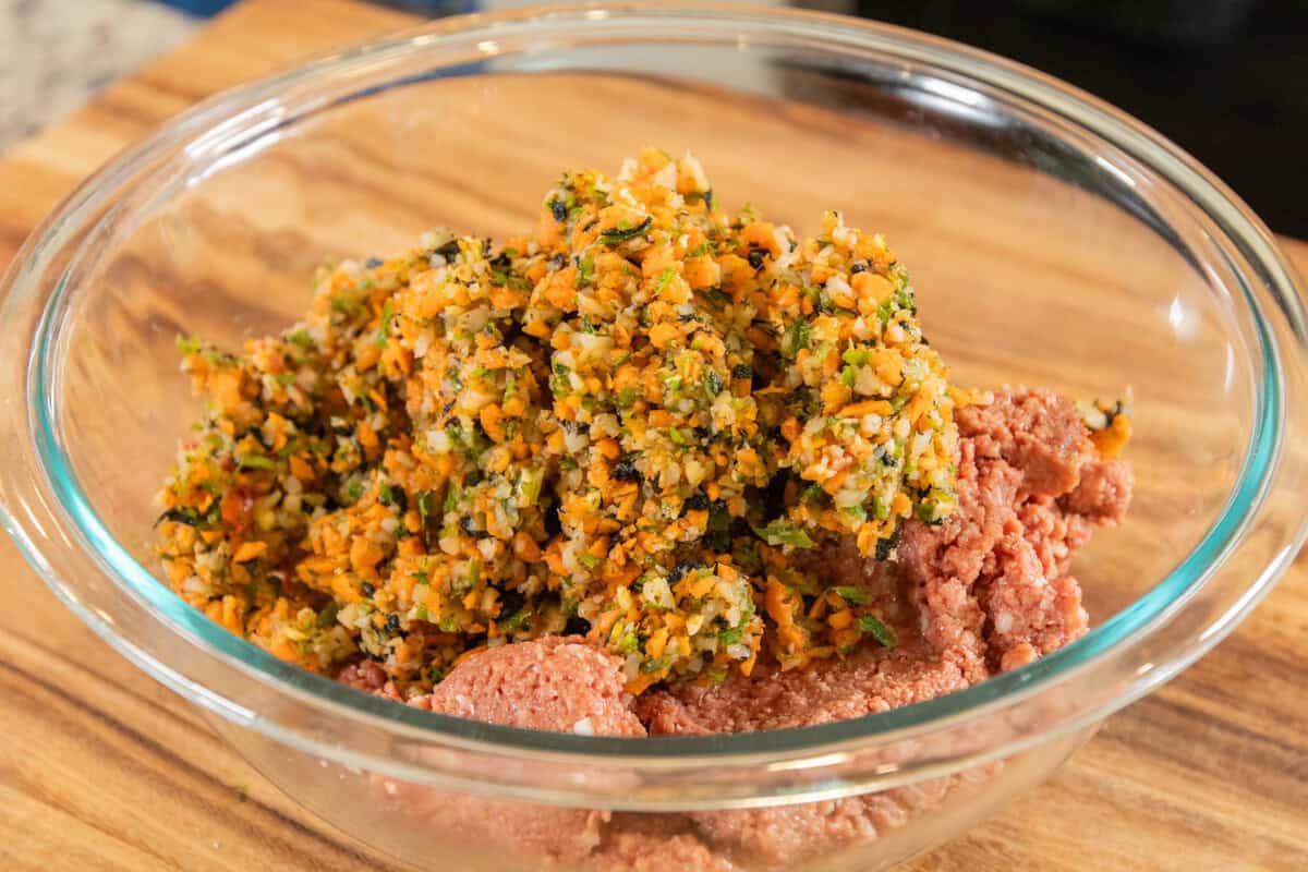 adding chopped veggies to the plant based ground in a medium bowl
