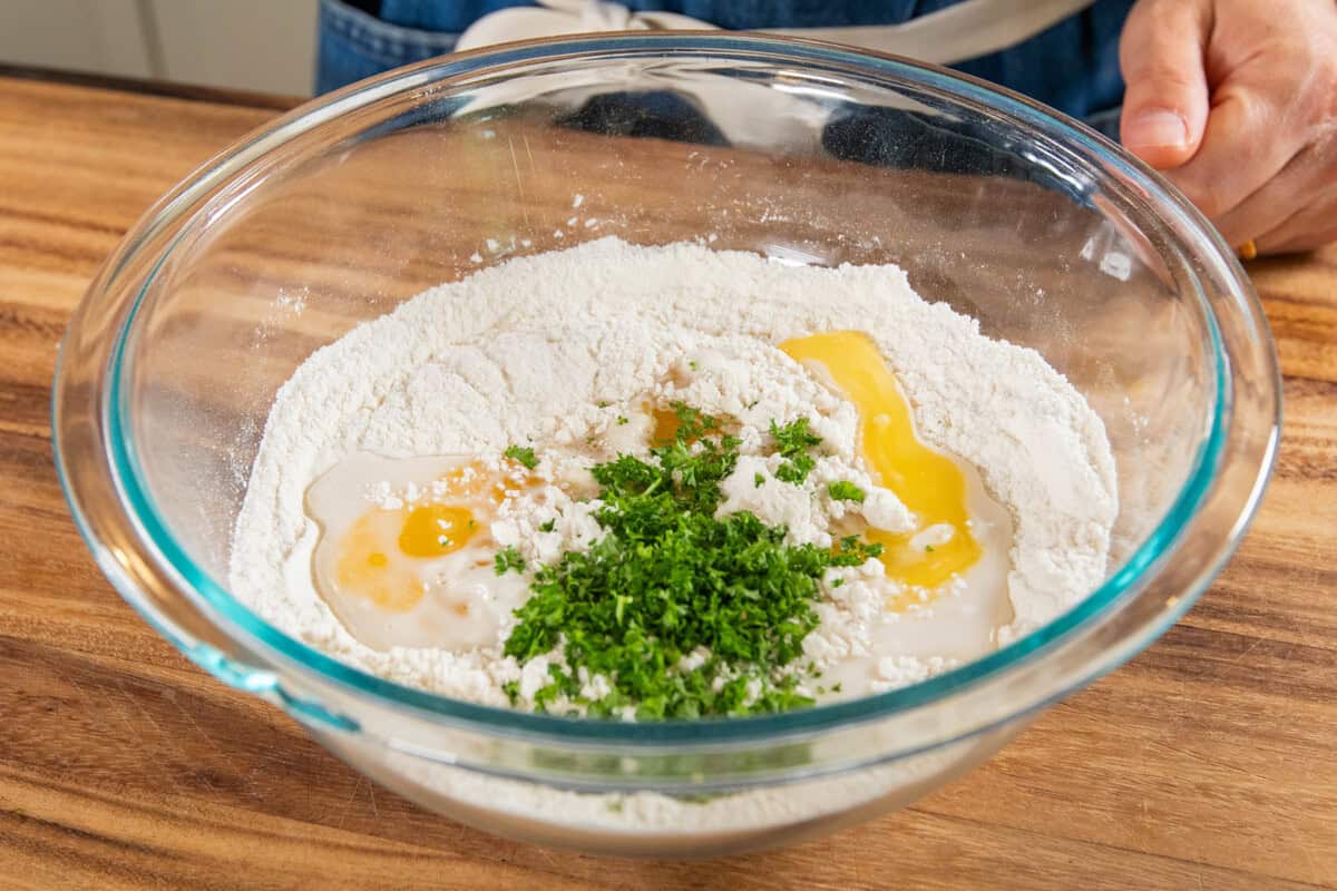 Vegan dough with herbs and eggs in a glass mixing bowl for baking or cooking.