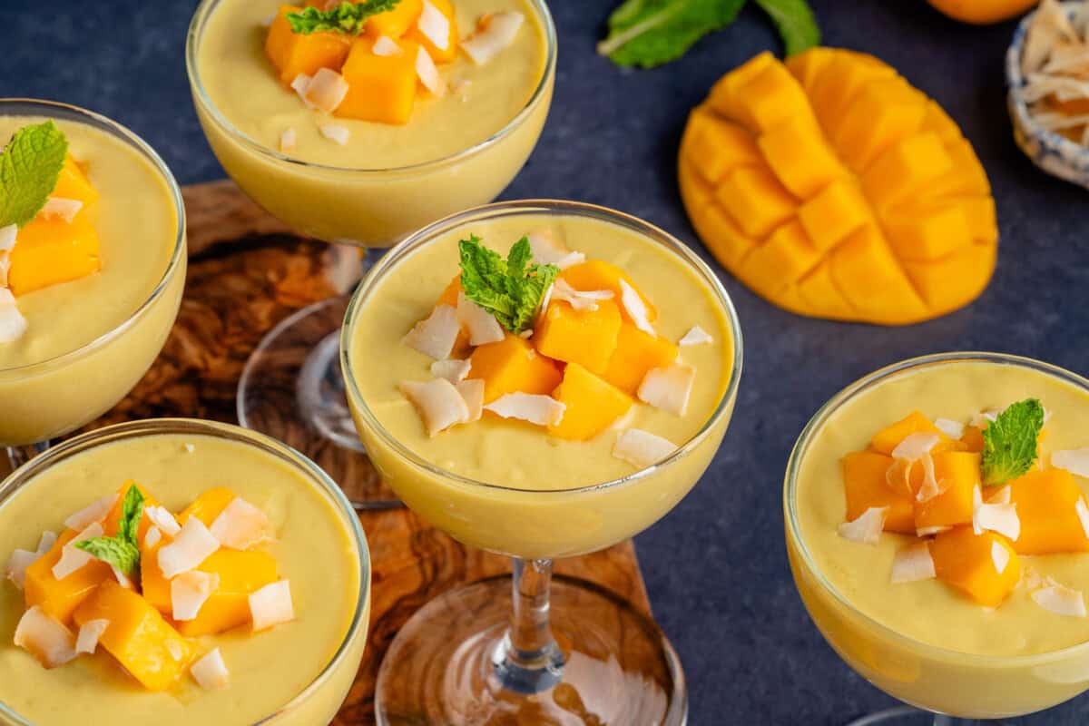 several glasses of mango posset topped with mango chunks, toasted coconut, and mint