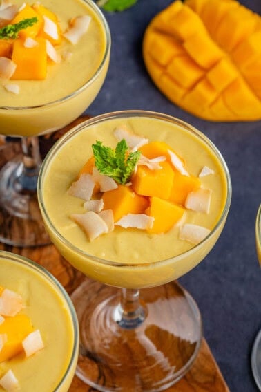 several glasses of mango posset topped with mango chunks, toasted coconut, and mint