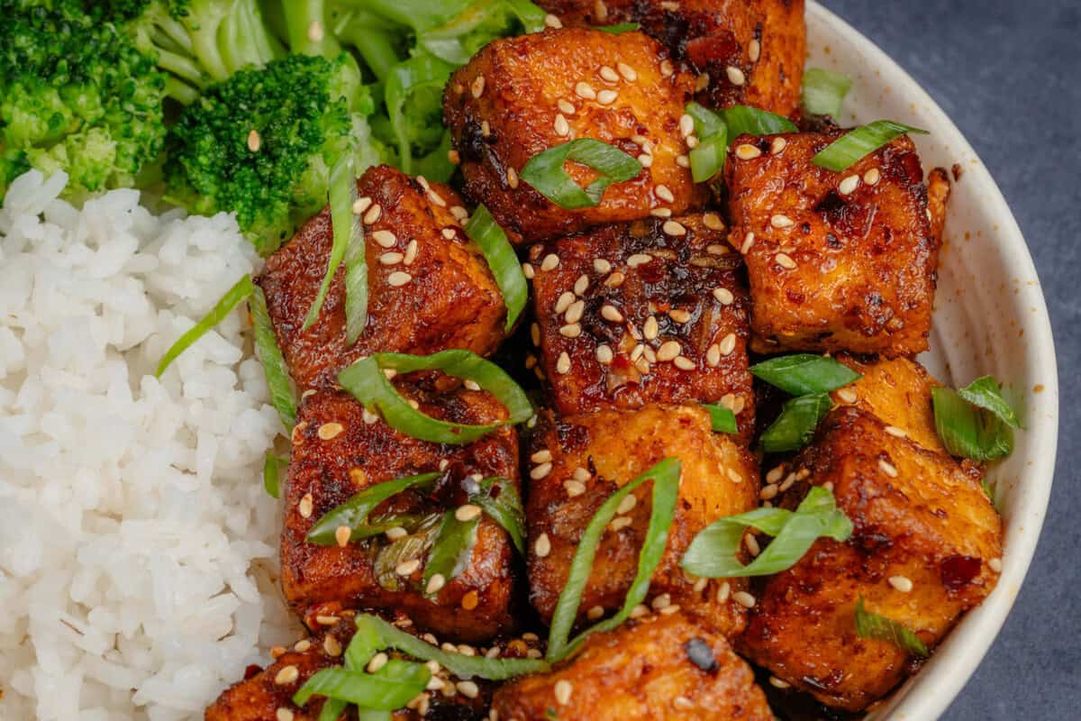 horizontal image of Chili Crisp Tofu in bowl with rice and broccoli, topped with scallions and toasted sesame seeds
