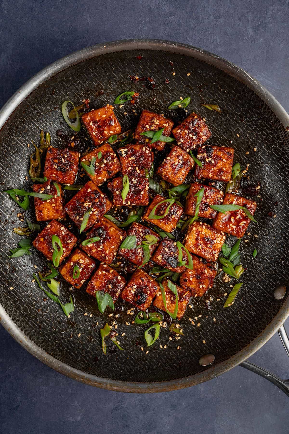 overhead photo of Chili Crisp Tofu cubes in pan with sliced green onions and toasted sesame seeds