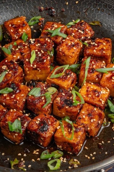 Chili Crisp Tofu cubes in pan with sliced green onions and toasted sesame seeds