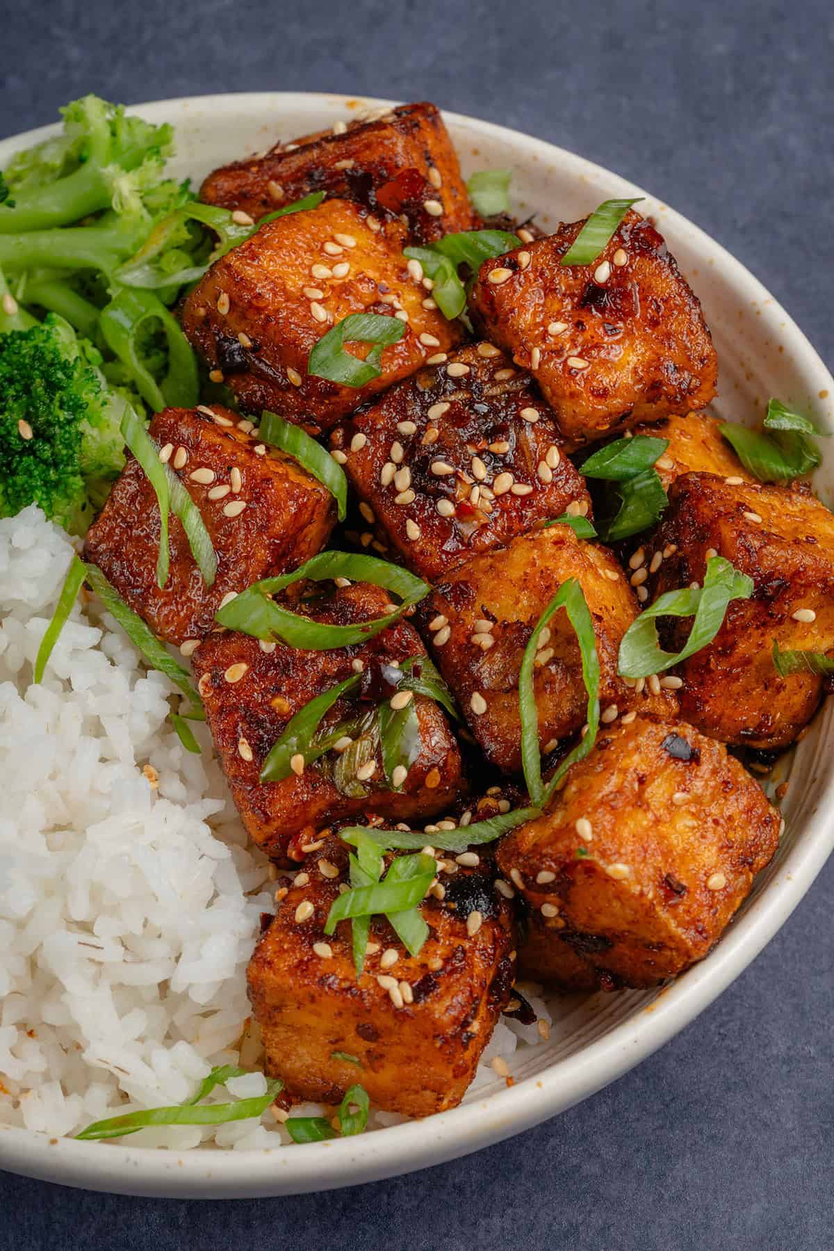 close up of Chili Crisp Tofu in bowl with rice and broccoli, topped with scallions and toasted sesame seeds
