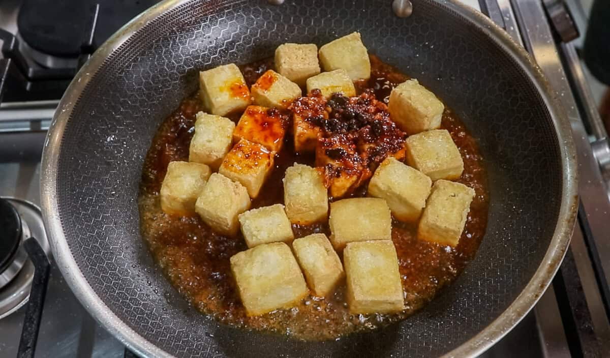 golden fried tofu in black pan with chili sauce on top