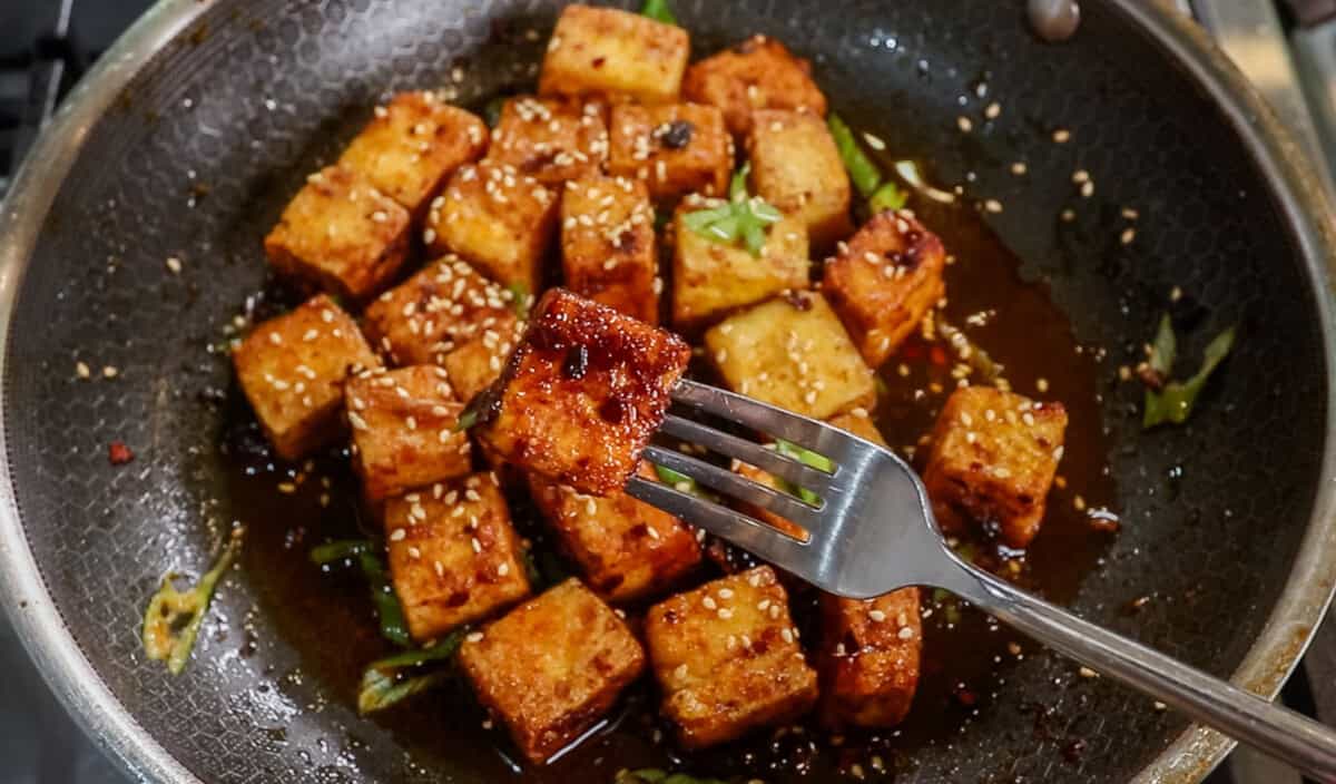 fork holding a cube of Chili Crisp Tofu over a pan