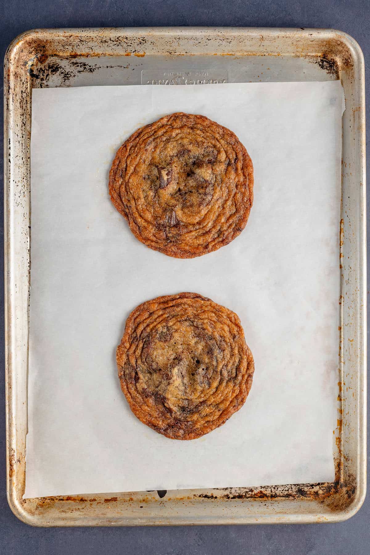 two thin crispy chocolate chip cookies on lined baking sheet